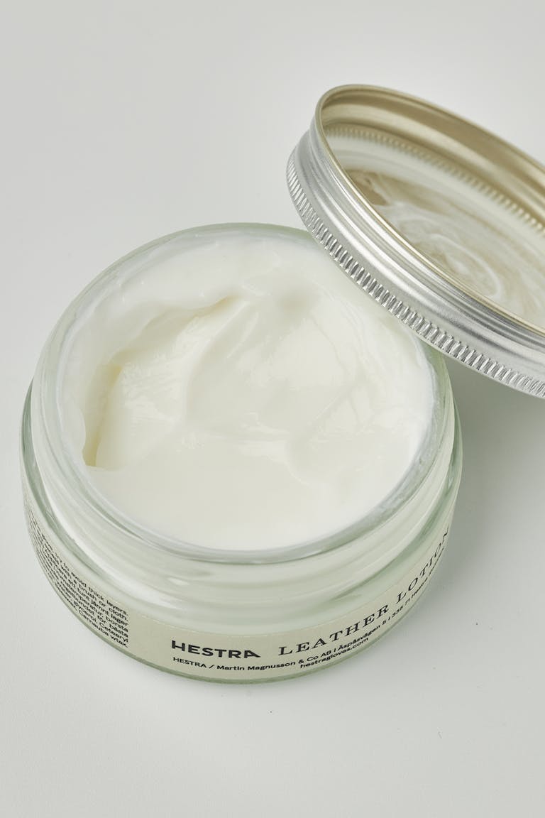L Ein Glas Lederbalsam für Handschuhe, geöffnet mit weißer Creme darin