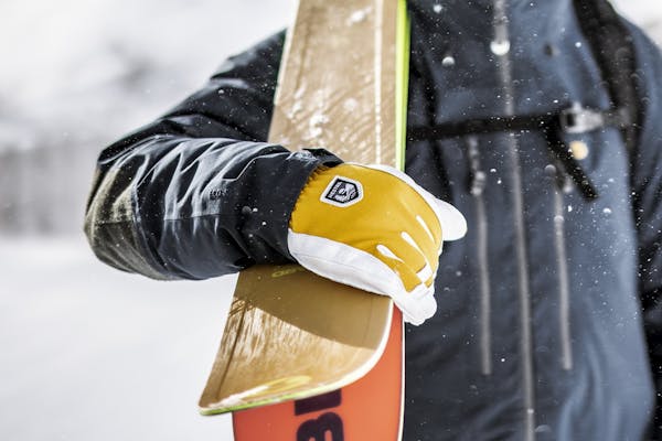 _D5A2275-Förbättrat-BR Eine Person trägt ein Paar Skier über der Schulter und trägt gelb-weiße Skihandschuhe