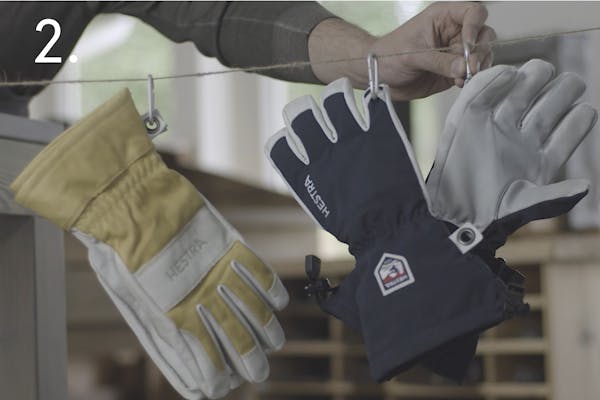 steg 2 sport En handskmakare hänger upp tre rengjorda skidhandskar på en lina med handskarnas karbinhakar i ett handskmakeri