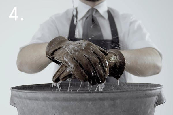 steg 4 dress En handskmakare sköljer av sina skinnhandskar under rinnande vatten över en balja i ett handskmakeri