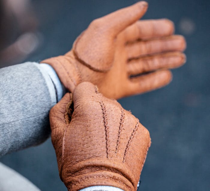 A person in stylish fall/winter attire putting on their light brown leather gloves