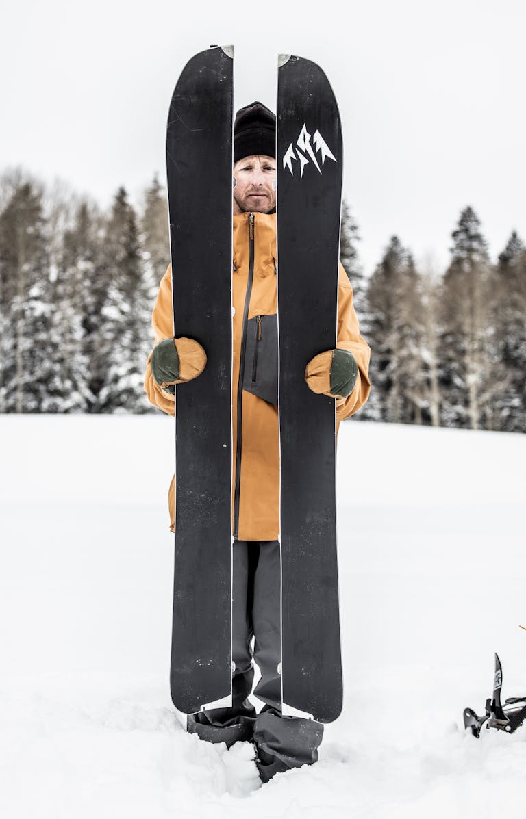 _E1A0671 En man håller i ett par splittrade skidor i snöig terräng, omgiven av vinterlandskap