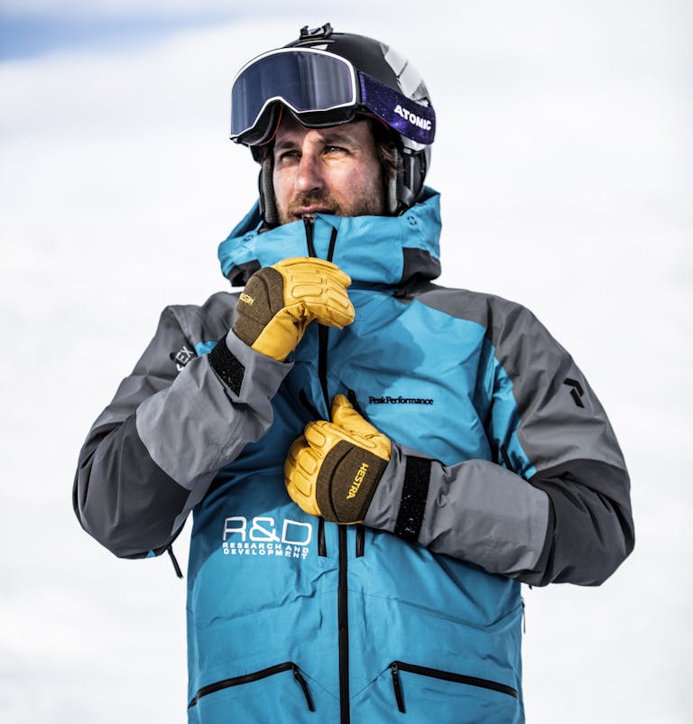 _E1A8202 (kopia) En man justerar sin jacka medan han bär skidutrustning i form av skidhjälm, skidglasögon och gula skidhandskar