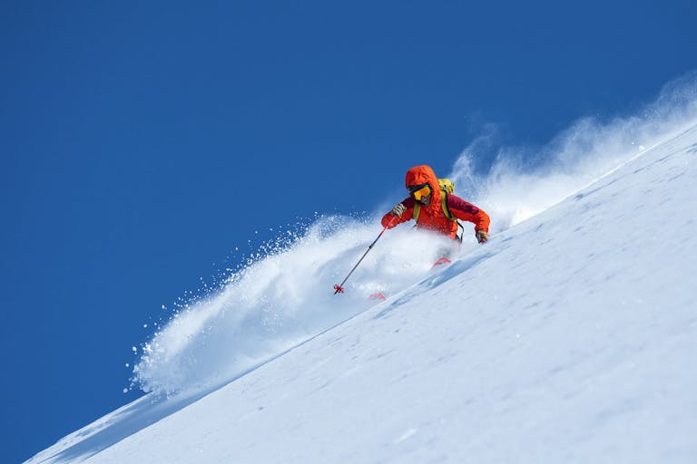 Chad Sayers, Blackcomb Mountain, British Columbia. Ein Skifahrer in roger Ausrüstung fährt einen verschneiten Hang hinunter bei klarem blauen Himmel