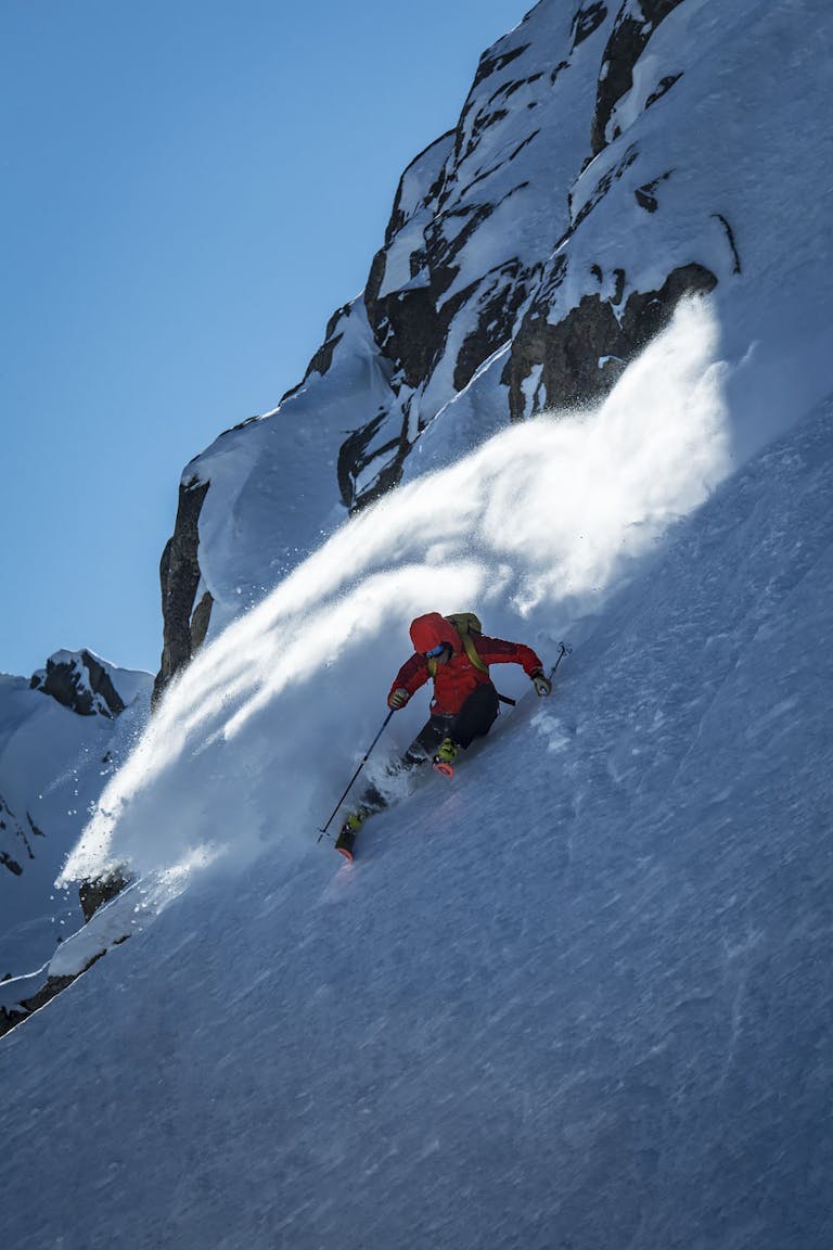 Chad Sayers, Whistler Mountain, British Columbia. Ein Skifahrer fährt einen steilen verschneiten Hang hinunter und hinterlässt eine Schneewolke an einem sonnigen Tag