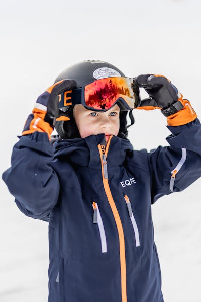 A playful child in ski clothing, putting on his snow googles during a winter day on the slopes
