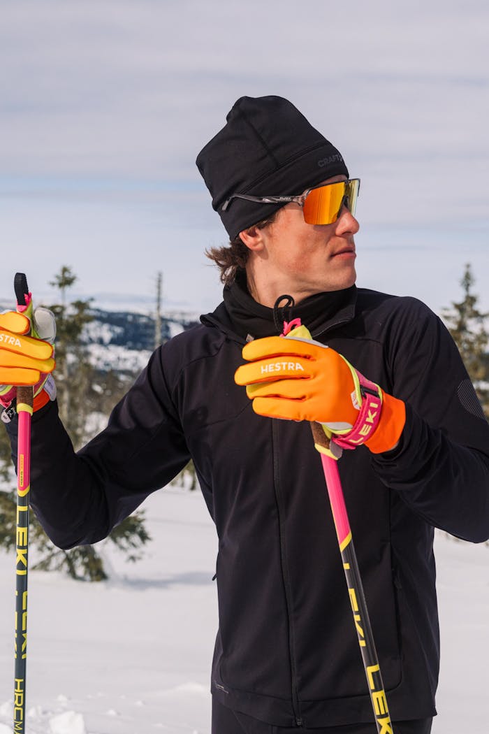 Ein Langläufer mit orangefarbenen Handschuhen bereitet sich auf das Skifahren in einer Winterlandschaft vor