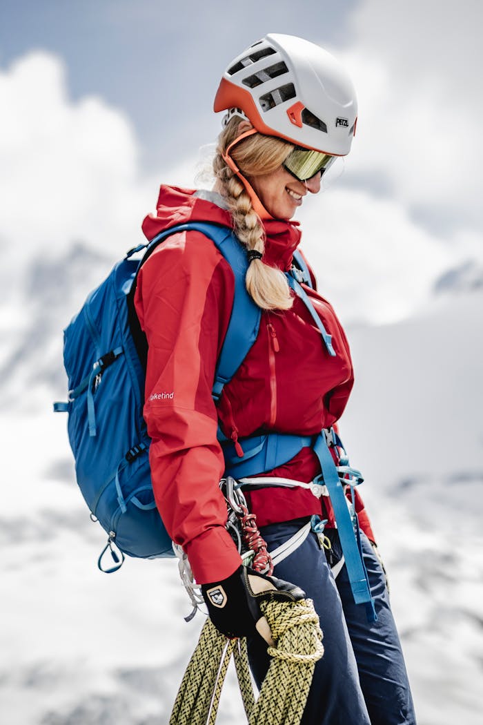 Eine Person mit technischen Handschuhen und Kleidung bedient Kletterausrüstung in einer alpinen Umgebung