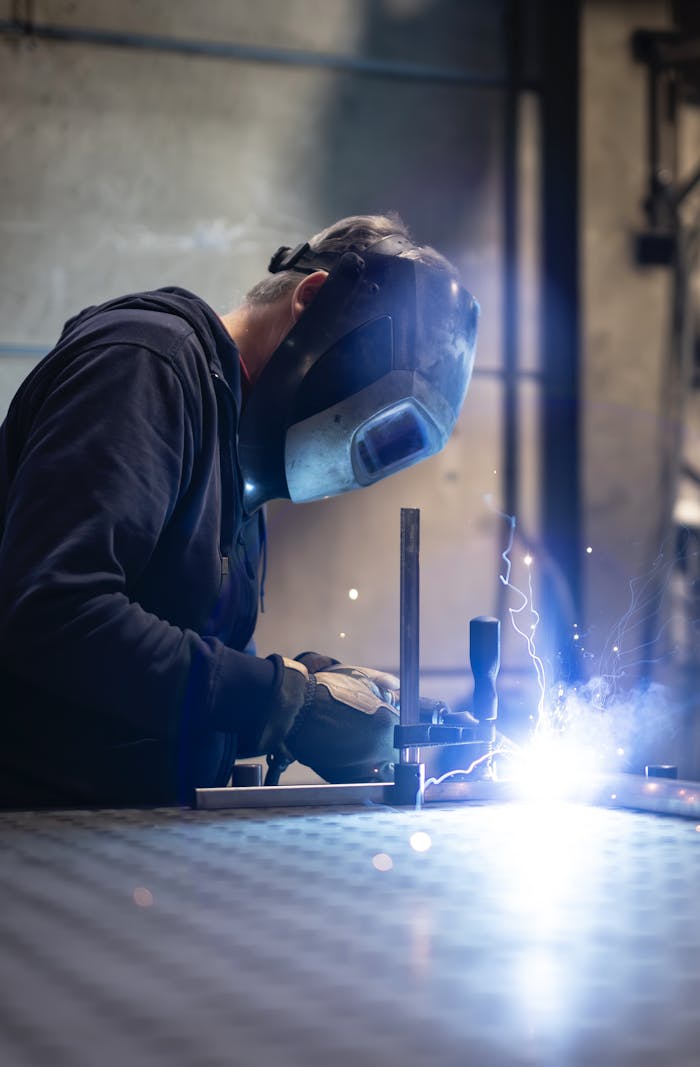 A man wearing protective gear welding inside a factory.