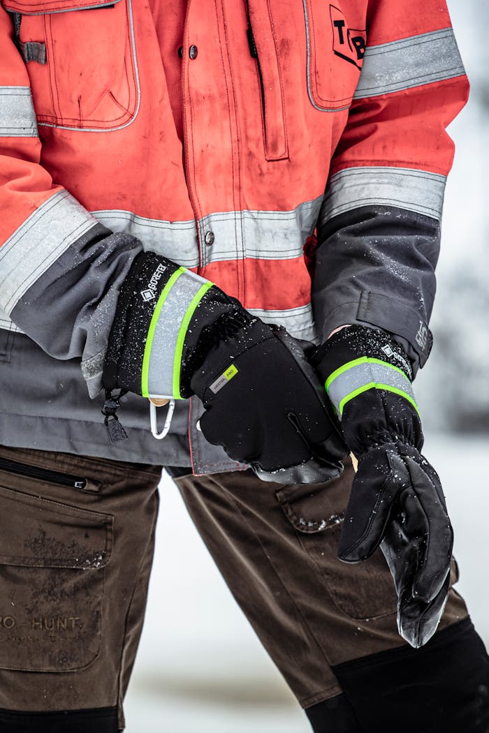 A man wearing a high-visibility jacket putting on a work glove in a winter setting.