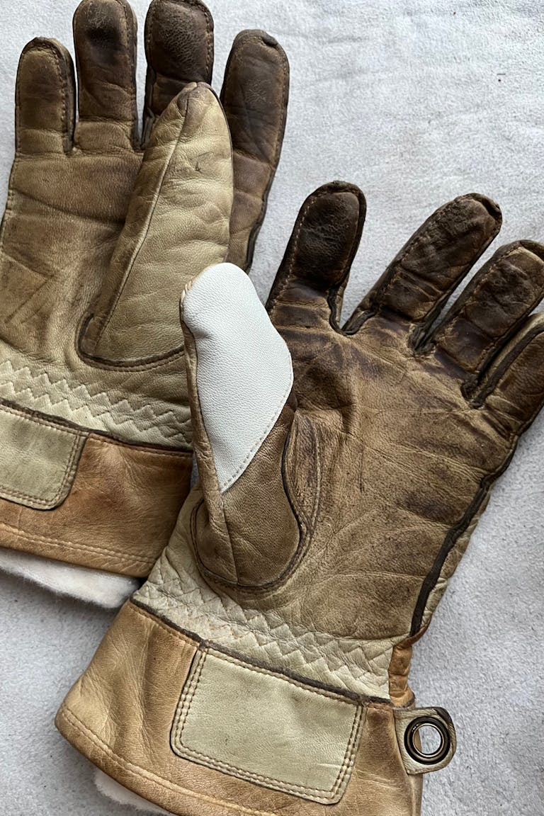 IMG_4477 Worn gloves with visible thumb repair, lying on a white surface