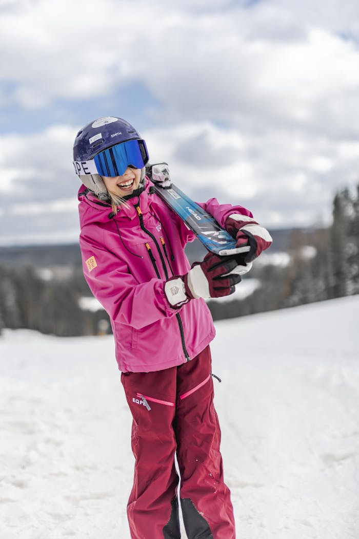 A playful child in ski clothing carries skis on their shoulder during a winter day on the slopes