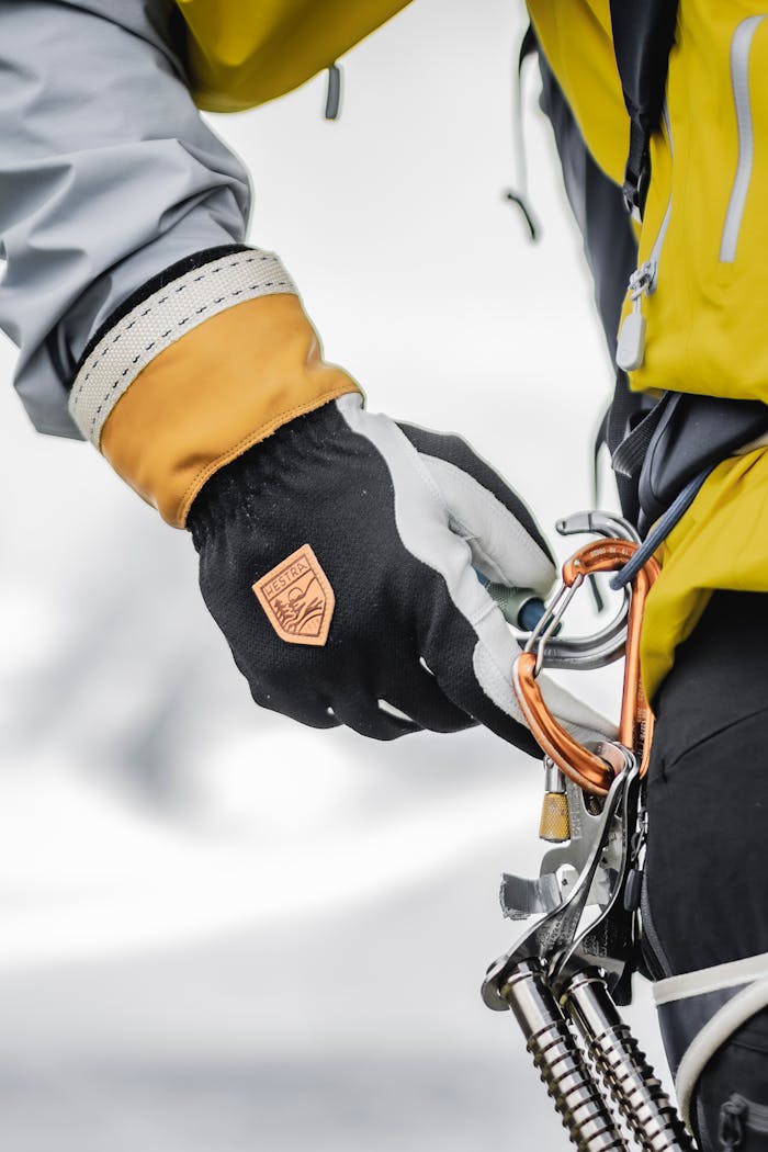 A person wearing technical gloves and clothing handles climbing gear in an alpine setting