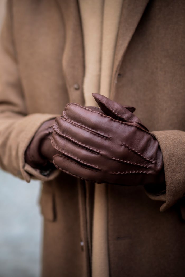 A person wearing brown leather gloves, paired with a brown winter coat in an urban setting