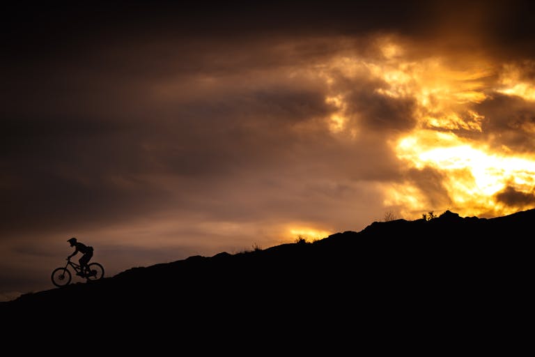 Syncline Day 2 A mountain biker in the distance riding down a trail as the sun sets